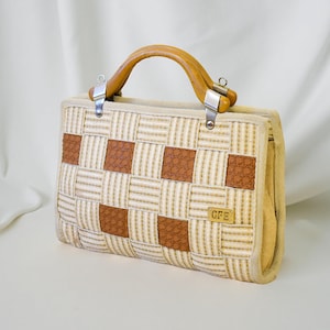 May include: A vintage handbag with a woven beige and brown pattern. It features a wooden handle and metal clasps. The initials "GFE" are on a small rectangular tag on the front of the bag.