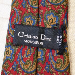 Pu&ograve; includere: Una cravatta di seta con motivo paisley rosso, blu e verde con un'etichetta nera che recita "Christian Dior Monsieur Made in Italy".