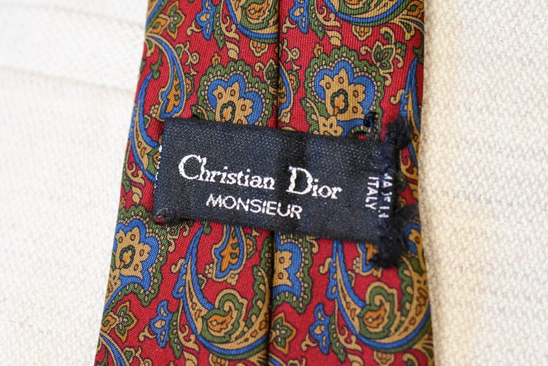 Pu&ograve; includere: Una cravatta di seta con motivo paisley rosso, blu e verde con un'etichetta nera che recita "Christian Dior Monsieur Made in Italy".