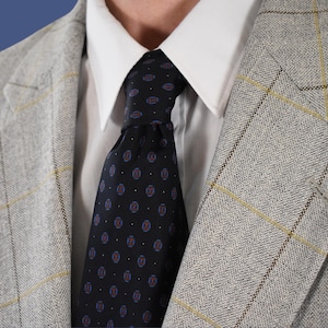 Può includere: Un blazer grigio con un sottile motivo a quadri e una cravatta blu scuro con motivo.