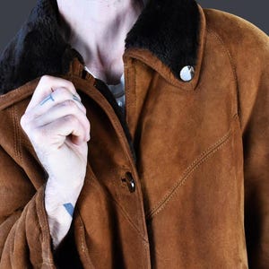 May include: A brown suede jacket with a black fur collar. The jacket has a button closure and a flap pocket on the chest.