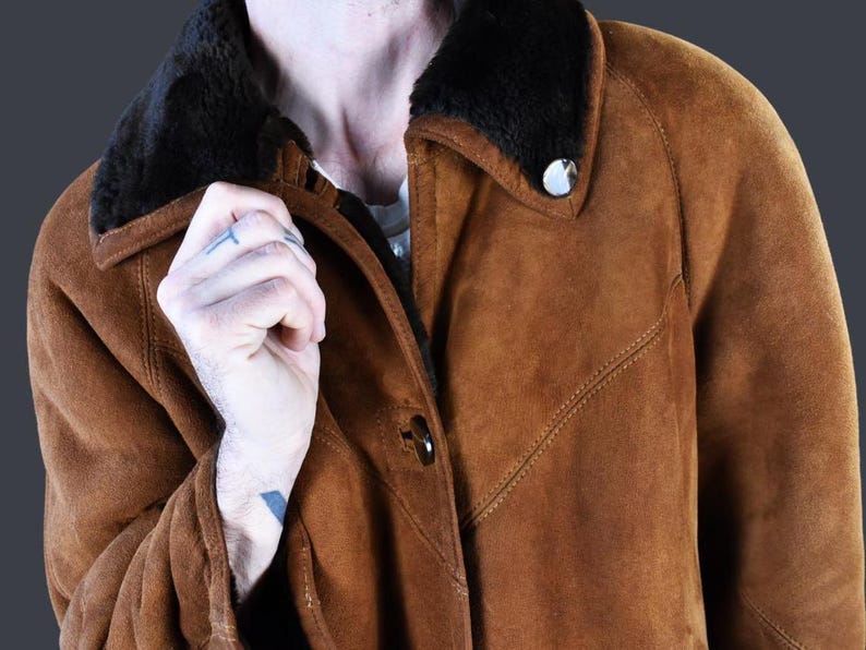 May include: A brown suede jacket with a black fur collar. The jacket has a button closure and a flap pocket on the chest.