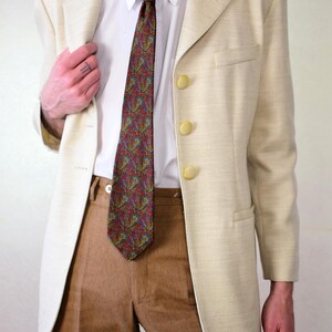 Pu&ograve; includere: Un blazer color crema con una cravatta a fantasia paisley e pantaloni di velluto a coste marroni. Il blazer ha tre bottoni dorati.