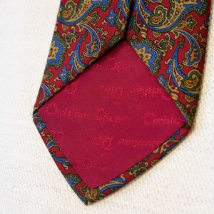 Pu&ograve; includere: Una cravatta di seta con motivo paisley rosso e verde con una fodera rossa su cui &egrave; scritto "Christian Dior" in lettere bianche.