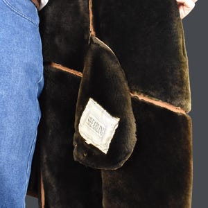 May include: A brown shearling jacket with a brown leather trim. The jacket is lined with a soft, black shearling fabric. The label on the jacket reads "Shearling".
