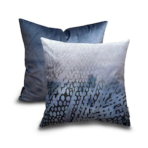 Puede incluir: Dos almohadas decorativas, una con tela de terciopelo azul sólido y la otra con un patrón abstracto azul y blanco.