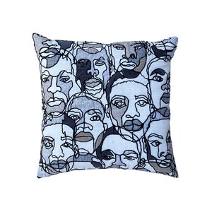 Puede incluir: Una almohada azul y blanca con un diseño bordado de múltiples dibujos de caras en líneas negras.