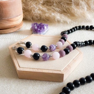 May include: Two beaded bracelets with black, pink, and purple beads. The bracelets are on a wooden display stand.