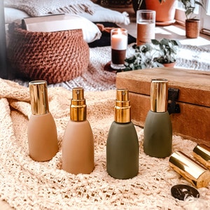 May include: Four glass bottles with gold tops and different colored liquids. The bottles are arranged in a row on a white crocheted surface.