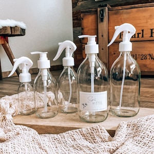Könnte beinhalten: Fünf durchsichtige Glasflaschen mit weißen Pumpen und Sprühdüsen. Die Flaschen sind mit Flüssigkeit gefüllt und haben Etiketten. Ein Etikett lautet "Spül Mittel - natural recipes".