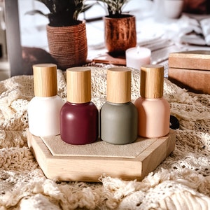 Op de afbeelding: Vier kleine glazen flesjes met bamboe deksels, elk gevuld met een andere kleur vloeistof. De flesjes zijn in een rij op een houten dienblad geplaatst, dat op een wit gehaakt kleed ligt.