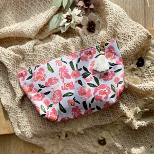 Op de afbeelding: Een witte ritszak met een roze bloemenpatroon en een witte kwast rits.