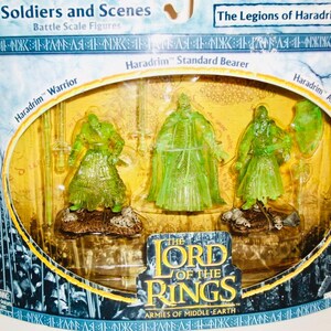Könnte beinhalten: Eine verpackte Reihe von durchscheinenden grünen Plastikfiguren aus The Lord of the Rings: Armies of Middle-earth. Das Paket enthält einen Haradrim-Krieger, einen Standartenträger und einen Bogenschützen. Die Verpackung trägt die Aufschrift "Soldiers and Scenes" und "The Legions of Haradrim."