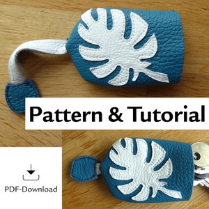 以下が含まれることがあります： 白い葉のデザインが施された、ティールレザーのキーフォブ。キーホルダーは白いストラップと端にティールアクセントが付いています。「Pattern & Tutorial」というテキストが画像に表示されています。