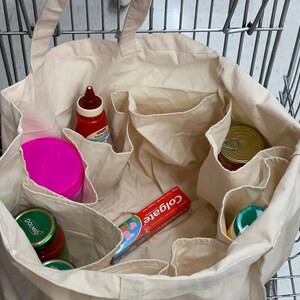 May include: A beige canvas tote bag with multiple compartments, filled with various grocery items, including a pink container, a red bottle of ketchup, a green jar labeled "Dolmio", a tube of Colgate toothpaste, and a can of food.