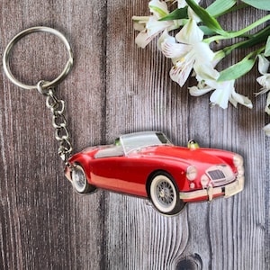 May include: A red convertible car keychain with a silver key ring. The car has a black interior and a chrome bumper.