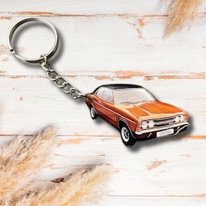 Op de afbeelding: Een sleutelhanger met een klassieke oranje auto met een zwart dak. De auto heeft zilveren sierlijsten en het woord "CORTINA" staat op de voorkant. De sleutelhanger heeft een zilveren ketting en ring.