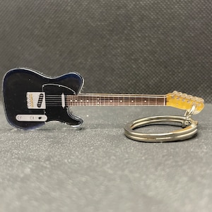 Puede incluir: Un llavero de guitarra eléctrica negra con un anillo de llave plateado. La guitarra tiene una golpeador cromado y una cabeza de afinación dorada.