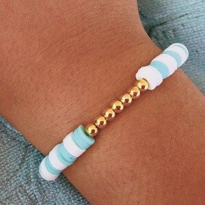 May include: A bracelet made of white and light blue beads with gold spacers.