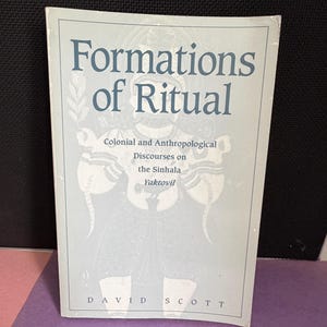 May include: A softcover book titled Formations of Ritual: Colonial and Anthropological Discourses on the Sinhala Yaktovil by David Scott. The cover is light gray with dark blue text and a faint, stylized illustration of a figure in the center.