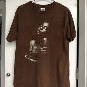 May include: A brown t-shirt with a white graphic print of a woman's face.