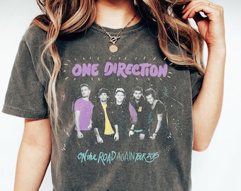 Peut inclure: Un t-shirt gris foncé avec un imprimé délavé du groupe One Direction en tournée. Le graphique comprend les membres du groupe et le texte "One Direction On The Road Again Tour 2015".