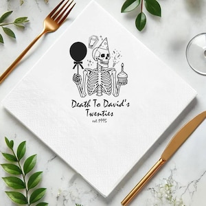 May include: White square paper napkin with a black skeleton illustration holding a balloon and cupcake. Text reads "Death To David's Twenties est.1995". Gold fork and knife are on the sides.