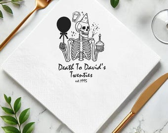 May include: White square paper napkin with a black skeleton illustration holding a balloon and cupcake. Text reads "Death To David's Twenties est.1995". Gold fork and knife are on the sides.