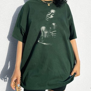 May include: A dark green oversized t-shirt with a black and white image of a woman's face on the front.