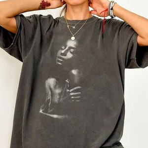 May include: A black t-shirt with a faded white graphic of a woman's face and shoulders.