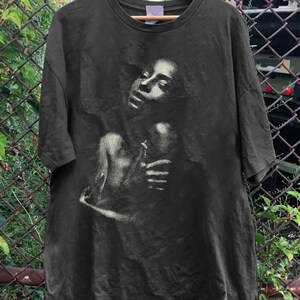 May include: A dark green t-shirt with a black and white image of a woman with her arms around herself.