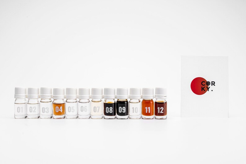 May include: Twelve small glass bottles with white caps, numbered 01 to 12, containing different colored liquids. A white card with a red circle and the text "COR KY." is to the right of the bottles.