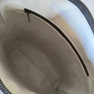 May include: The inside of a black zippered bag with a white fabric lining. The bag has a zippered pocket on the inside.
