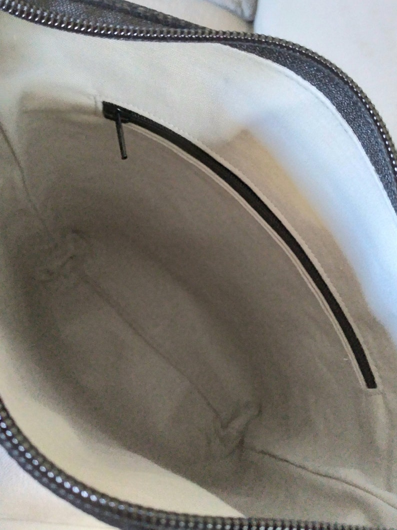 May include: The inside of a black zippered bag with a white fabric lining. The bag has a zippered pocket on the inside.