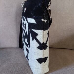 May include: A black and white patterned crossbody bag with a black suede flap and a silver chain strap. The bag has a fringe detail and a silver concho.