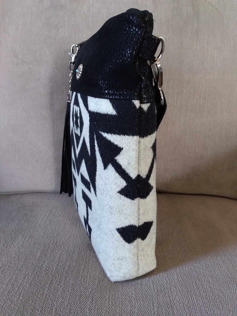 May include: A black and white patterned crossbody bag with a black suede flap and a silver chain strap. The bag has a fringe detail and a silver concho.