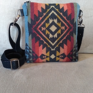 May include: A small crossbody bag with a black strap and a colorful geometric pattern. The pattern features shades of red, orange, yellow, blue, and black.