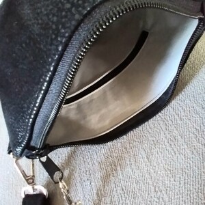 May include: A black zippered pouch with a silver chain strap. The pouch has a white lining and a small seashell design on the front.