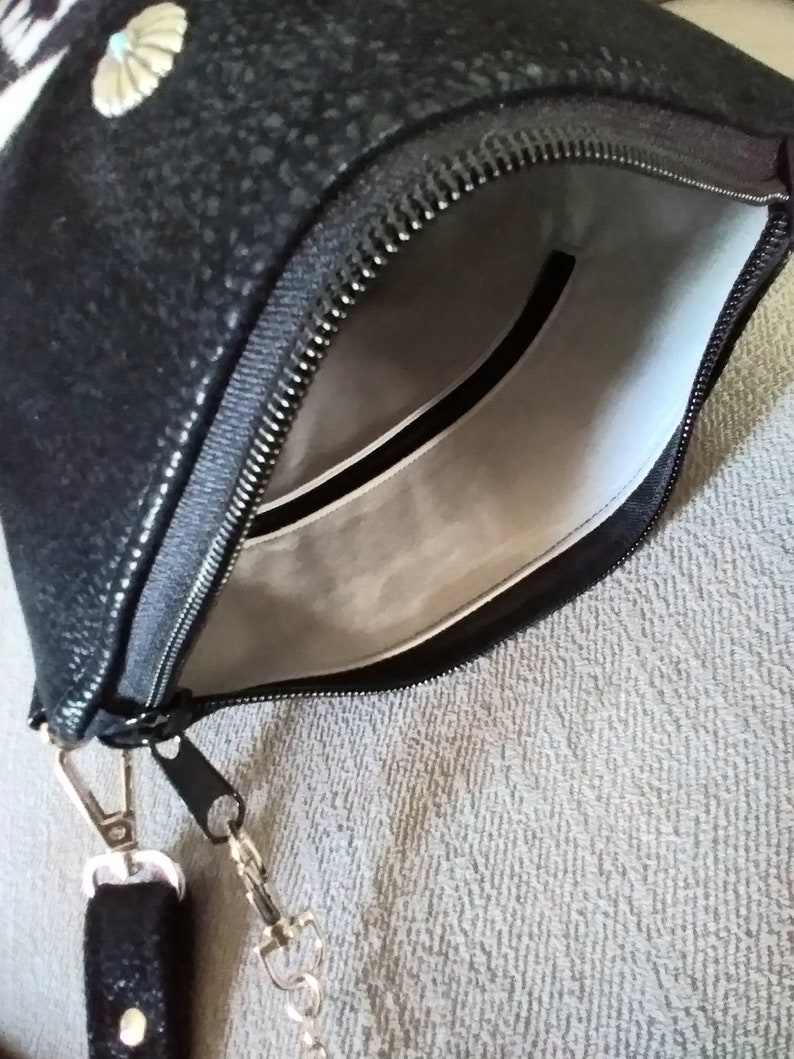 May include: A black zippered pouch with a silver chain strap. The pouch has a white lining and a small seashell design on the front.