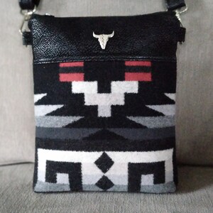 May include: Black leather crossbody bag with a silver bull skull charm. The bag features a black, white, and red geometric pattern.