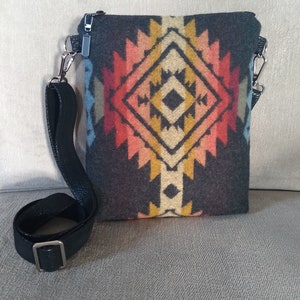 May include: A small black crossbody bag with a colorful geometric pattern. The bag has a black adjustable strap and a silver zipper.