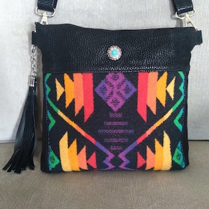 May include: Black leather crossbody bag with a colorful geometric patterned flap. The bag has a silver chain and tassel.