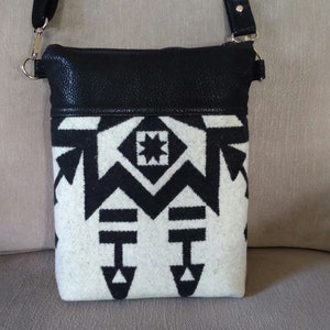 May include: A black and white geometric patterned crossbody bag with a black leather flap. The bag has a silver chain strap.