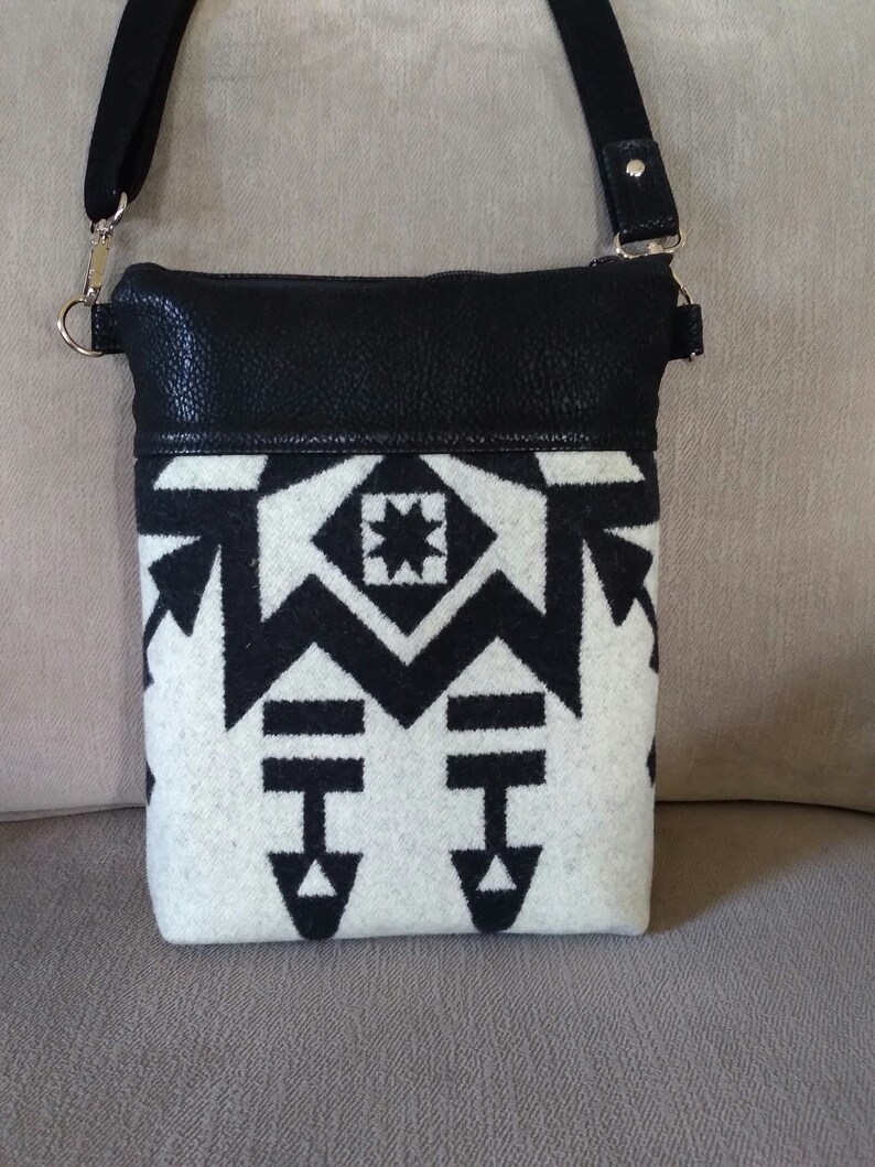 May include: A black and white geometric patterned crossbody bag with a black leather flap. The bag has a silver chain strap.