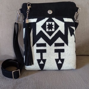 May include: Black and white geometric patterned crossbody bag with a black leather strap and tassel. The bag has a black suede flap with a turquoise stone embellishment.