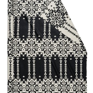 May include: A black and white patterned throw blanket with a geometric design. The blanket is rolled up and ready to be used.