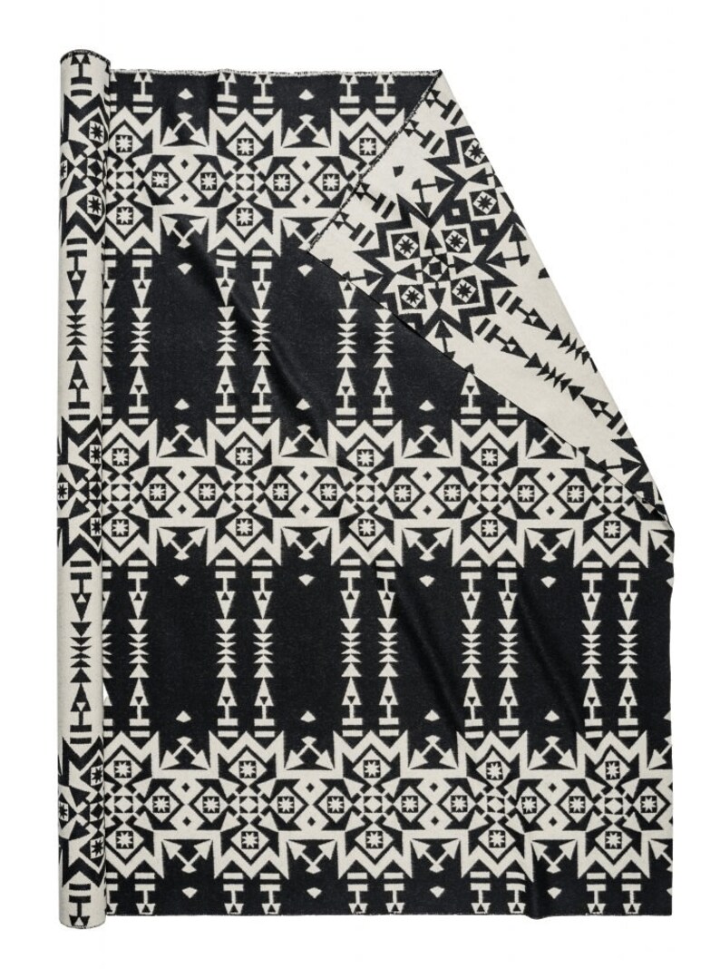 May include: A black and white patterned throw blanket with a geometric design. The blanket is rolled up and ready to be used.