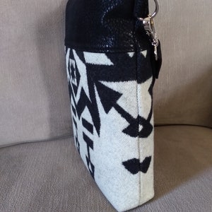 May include: A black and white patterned crossbody bag with a black faux leather flap and a silver clasp. The bag has a geometric design.