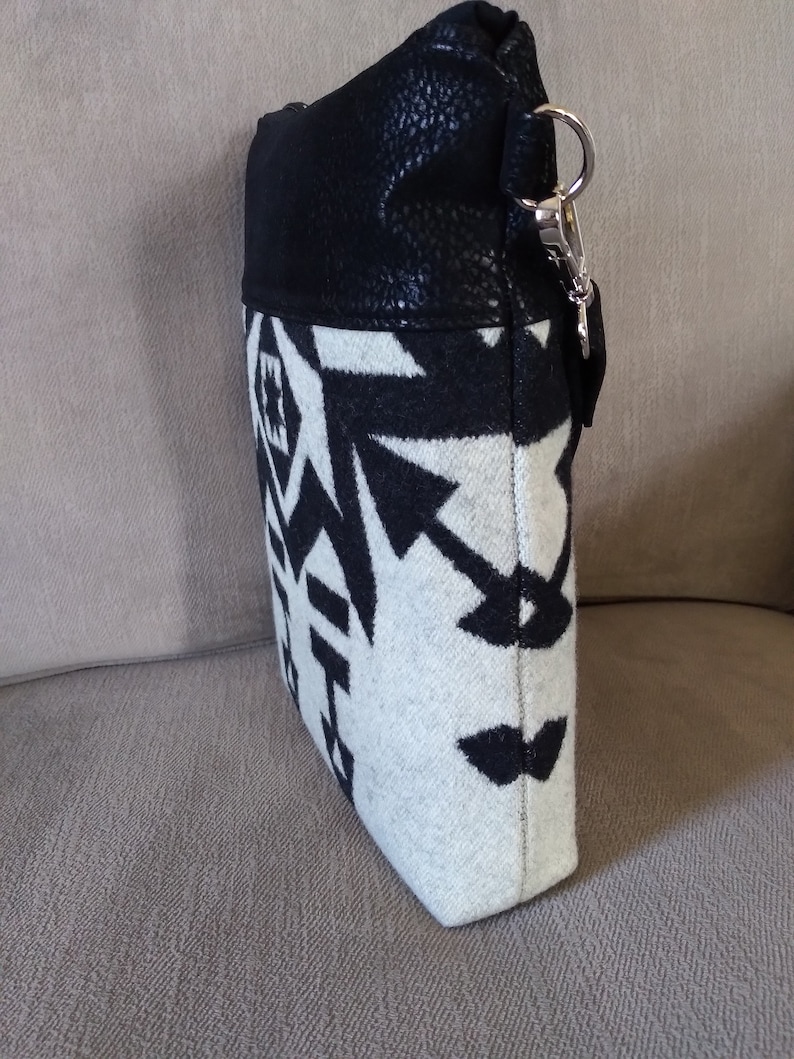 May include: A black and white patterned crossbody bag with a black faux leather flap and a silver clasp. The bag has a geometric design.