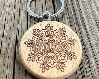 May include: Wooden keychain with a floral design and the word "Nurse" engraved on it. The keychain is attached to a silver key ring.